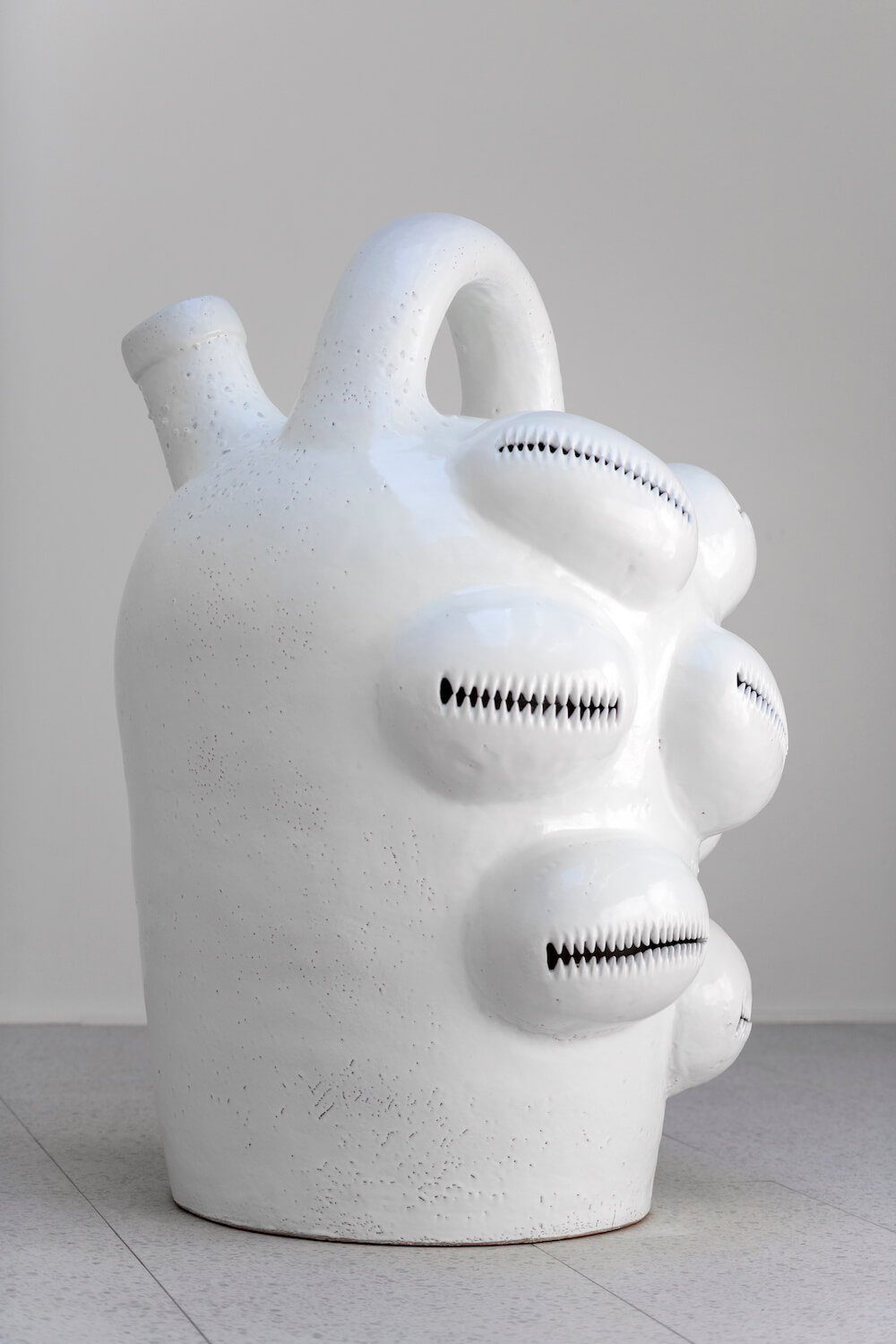 A large white sculpture of a jug with cowrie shells