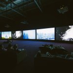An installation of six screens featuring video stills of soft, blue landscapes in a dark room